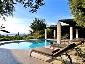 Zona de piscina con sillones de descanso, una mesa con una bebida y vista al mar.