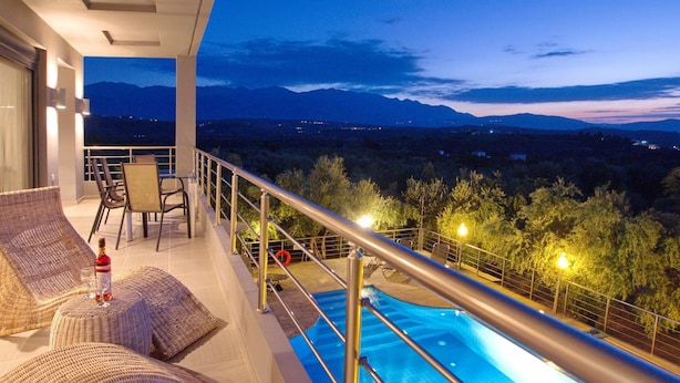 Un balcón con piscina, mobiliario de mimbre y vistas a las montañas al atardecer.