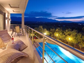 A balcony with a pool, wicker furniture, and a view of mountains at dusk. - Villa Kallisto in Almyrida (Apokoronas)
