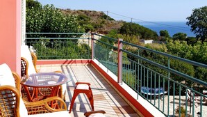 A balcony with wicker furniture, a glass table, and a view of the sea and hills. - Villa Emiliata in Spartia (Kefalonia)