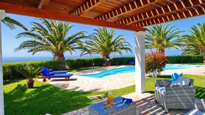 A covered outdoor area with a pool, lounge chairs, and a view of the ocean. - Villa Ermis in Spartia (Kefalonia)