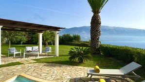 A pool area with stone tiles, lounge chairs, a pergola, and a view of the sea and mountains. - Villa Ermis in Spartia (Kefalonia)