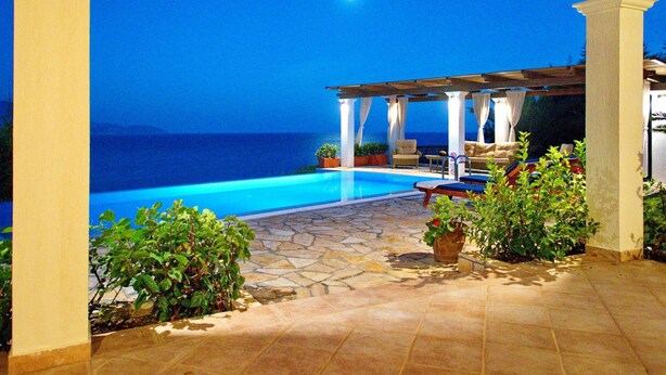 A covered outdoor pool area with a view of the ocean at night. - Villa Penelope in Spartia (Kefalonia)