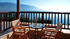 A balcony with a glass table and two chairs, overlooking a body of water and mountains. - Villa Penelope in Spartia (Kefalonia)