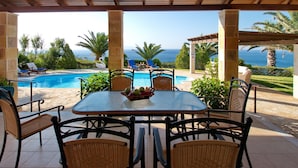 A covered outdoor area with a pool, lounge chairs, and a table with fruit. - Villa Kephalos in Spartia (Kefalonia)