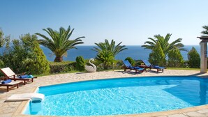 A swimming pool with lounge chairs and a swan statue, surrounded by palm trees and a view of the sea. - Villa Kephalos in Spartia (Kefalonia)