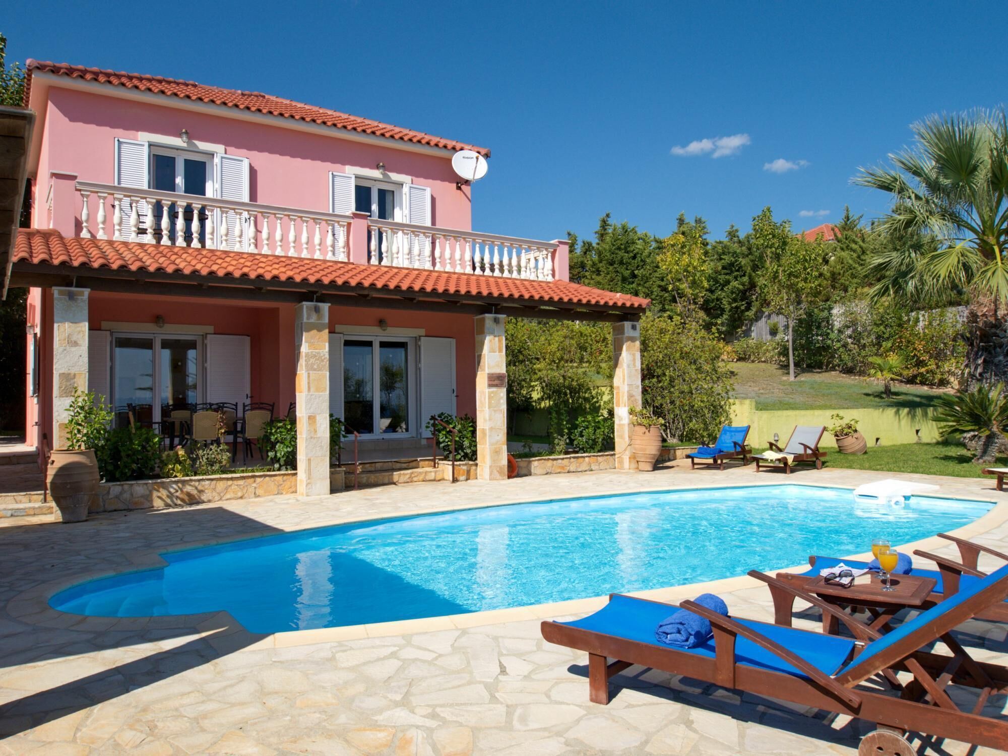 A pink villa with a swimming pool, lounge chairs, and a garden.