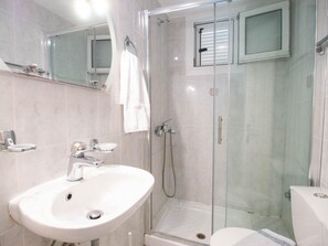 Moderni kylpyhuone, jossa on lasiseinällä varustettu suihku, valkoinen pesuallas ja wc.
