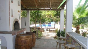 A covered outdoor area with stone flooring, wooden barrels, and a barbecue setup. - Maros Spitaki in Varipetro (Chania)