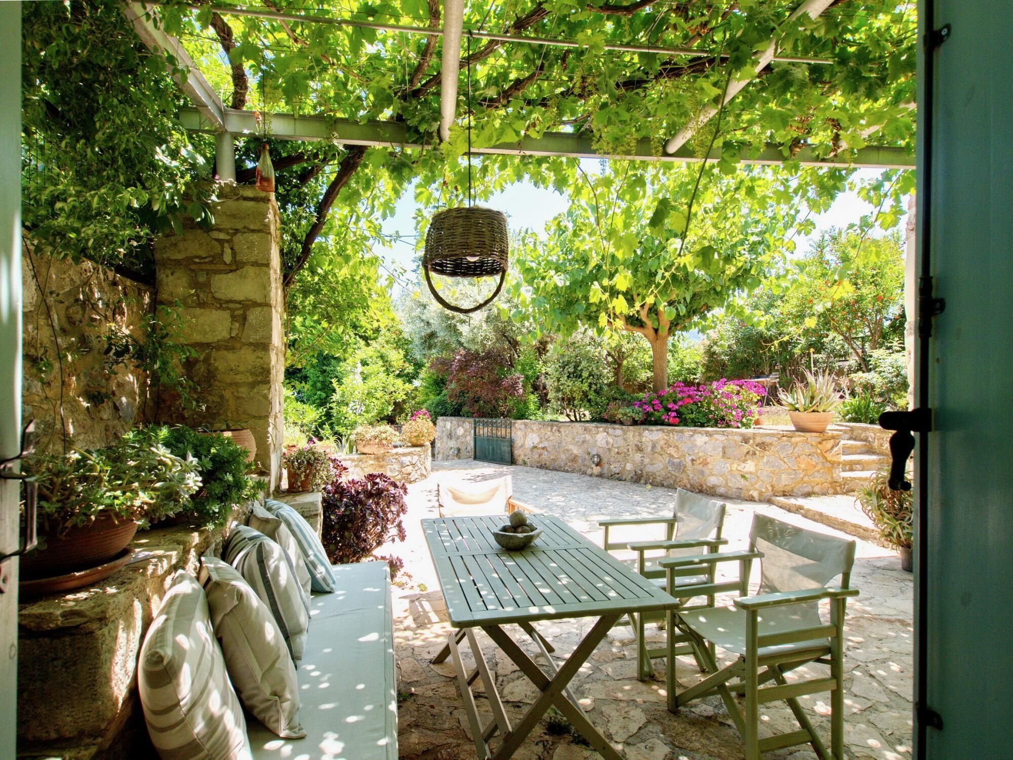 An outdoor patio with a stone wall, a wooden table, and chairs.