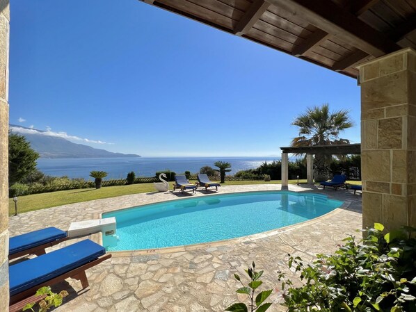 Zona de piscina con vista al mar, sillas de descanso y un pérgola.
