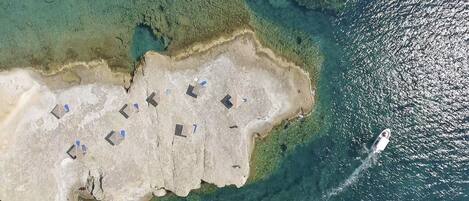 Oversigtsbillede af et kystområde med en sandstrand og flere små bygninger, måske hytter eller både, der ligger i en række.