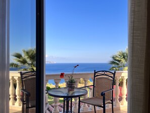 Un balcon avec une table et des chaises, offrant une vue sur la côte, avec des palmiers et un ciel dégagé.