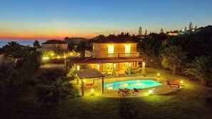 A two-story house with a swimming pool, surrounded by palm trees and a view of the sea at dusk. - Villa Dionysos in Spartia (Kefalonia)