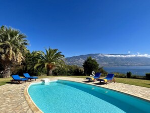 Una piscina con sillas reclinables azules, palmeras y vista a la montaña.