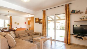A living room with a sofa, a coffee table, a TV, and a sliding glass door to the outside. - Villa Hephaestus in Spartia (Kefalonia)