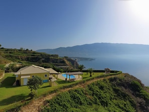 Ein Küsteneigentum mit Pool, einem kleinen Gebäude und Blick auf Meer und Berge.