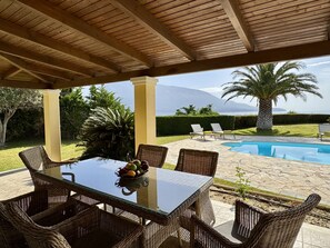 An outdoor patio with a glass table, wicker chairs, a pool, and a view of mountains. - Villa Hephaestus in Spartia (Kefalonia)