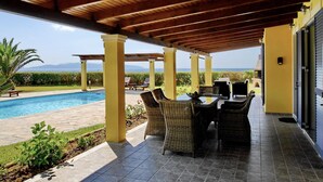 A covered outdoor area with a pool, wicker furniture, and a view of the ocean. - Villa Hephaestus in Spartia (Kefalonia)