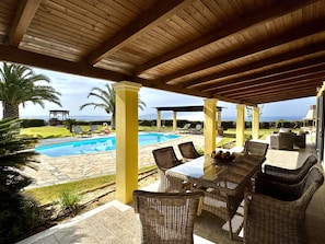 A covered outdoor area with a pool, wicker furniture, and a view of the sea. - Villa Hephaestus in Spartia (Kefalonia)