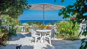An outdoor patio with a table and chairs, a white umbrella, and a view of the sea. - Rouladina Apt 4 in Stalos (Chania)