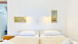 A hotel room with two beds, a bathroom with a glass shower, and artwork on the walls. - Rouladina Apt 4 in Stalos (Chania)