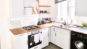 Une cuisine moderne avec des meubles blancs, un plan de travail en bois, une cuisinière à gaz, un four encastré, un lave-linge et une fenêtre avec vue.