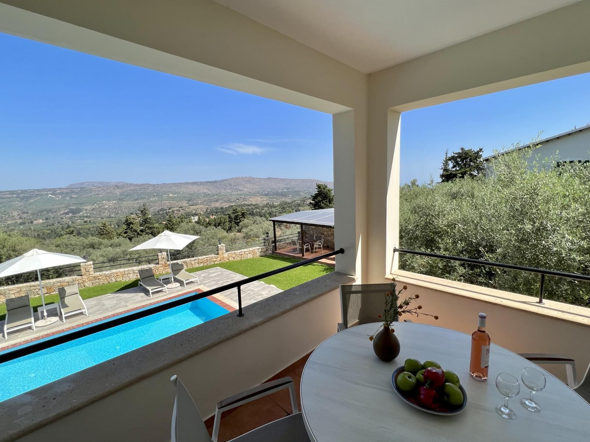 A balcony with a pool, outdoor seating, and a table with fruit and wine glasses.