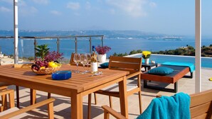 An outdoor dining area with a table set for two, overlooking a scenic view of the sea and distant land. - Villa Nikos in Megala Chorafia (Chania)