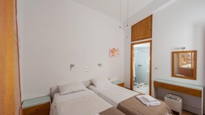 Een slaapkamer met twee bedden, een houten garderobe, een douchecabine met glazen wanden en een houten bureau met spiegel.