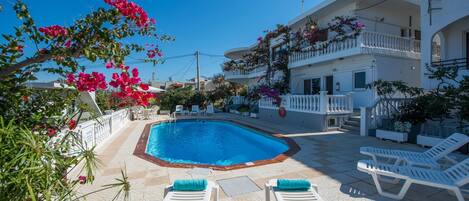 A swimming pool with white lounge chairs and a white building with balconies.