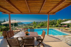 Ein überdachter Außenbereich mit Pool, Holzmöbeln und Blick auf die Landschaft.