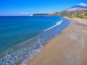 Ein Strand mit klarem, blauem Wasser, einem sandigen Ufer und einem Berg im Hintergrund.
