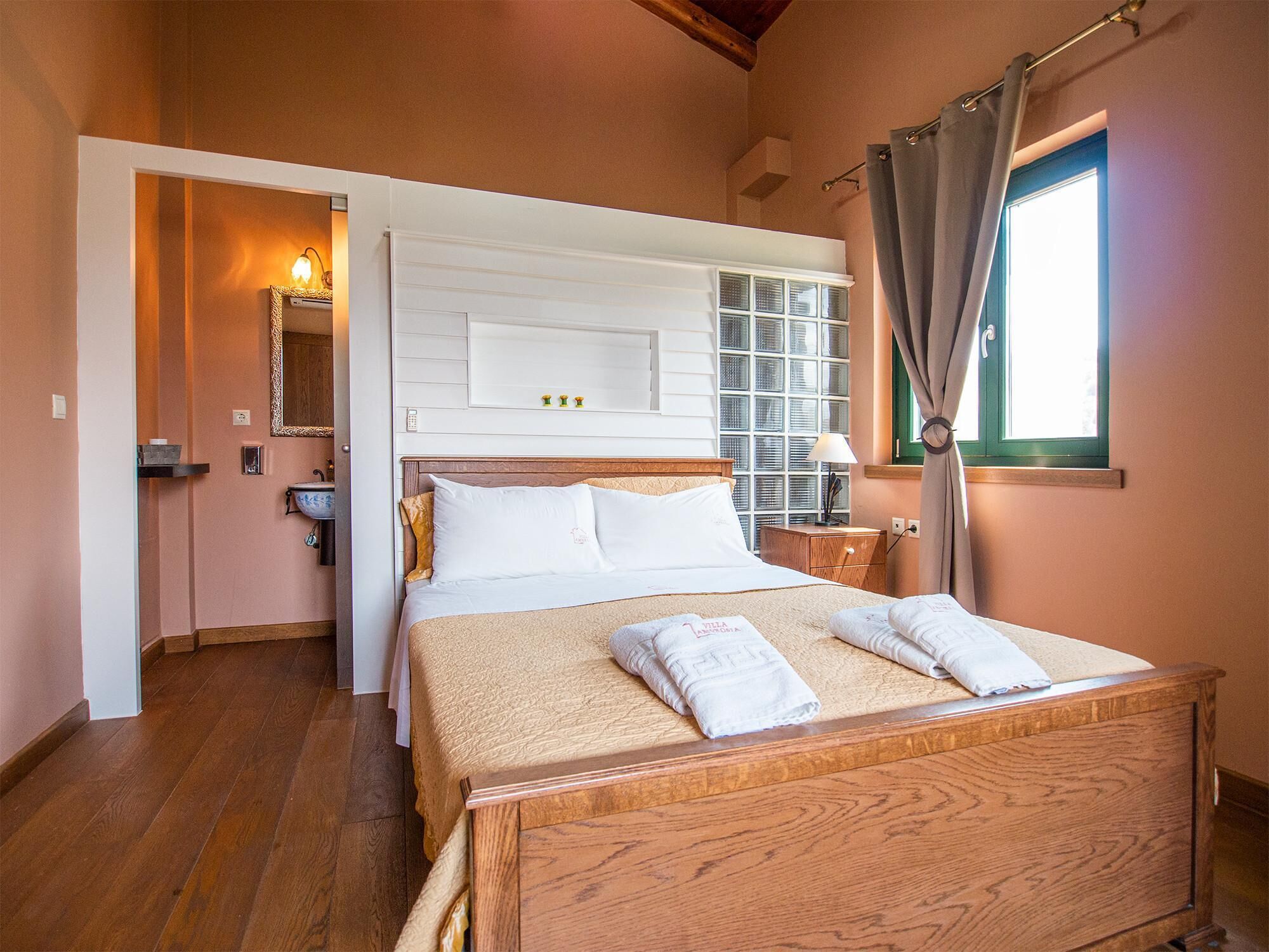 Een slaapkamer met een houten bed, wit beddengoed, een nachtkastje met een lamp, een raam met gordijnen en een spiegel aan de muur.