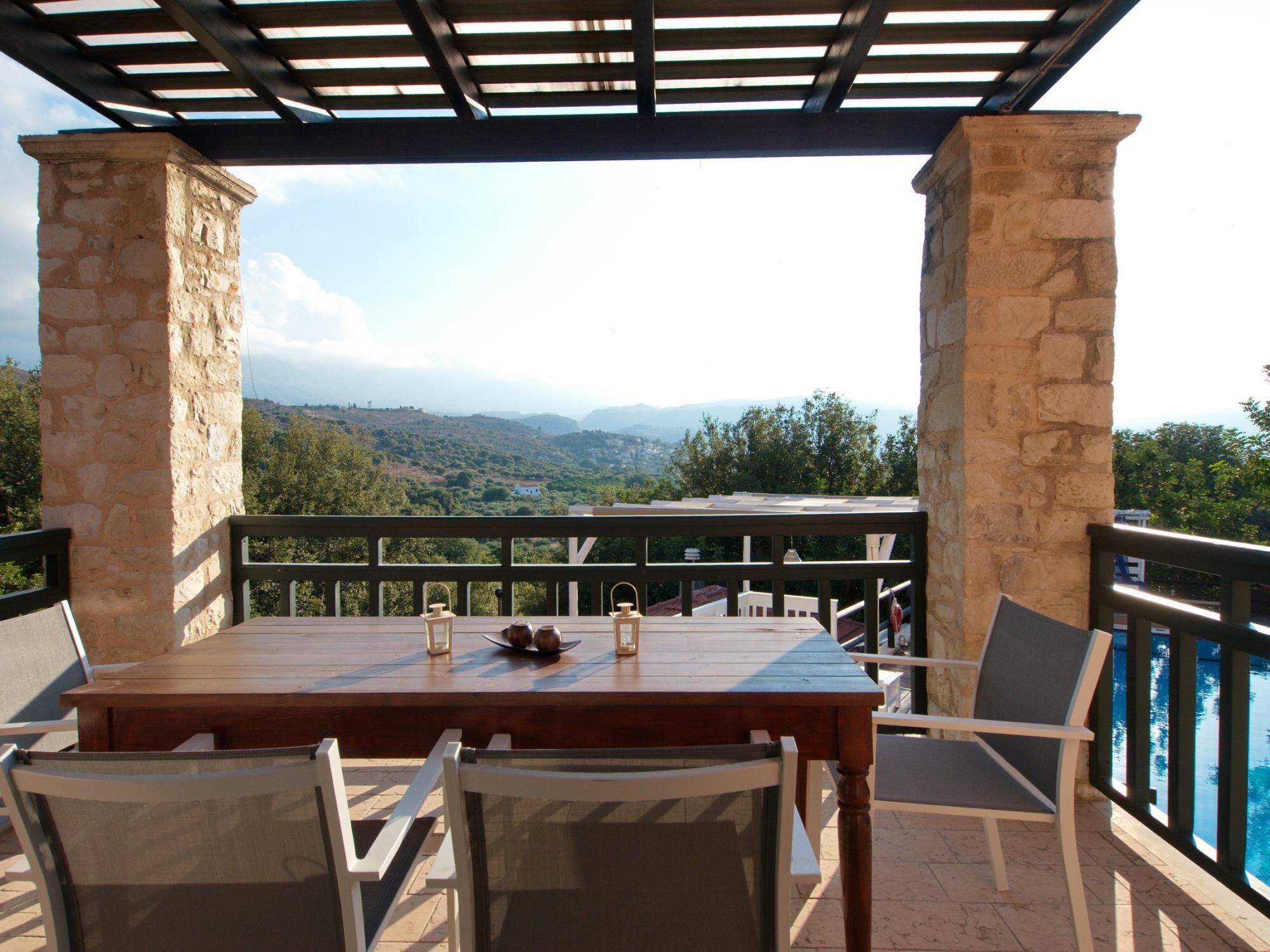 A covered outdoor seating area with a table and chairs, stone pillars, and a view of a mountainous landscape.