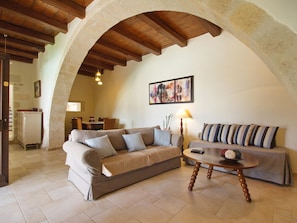 Uma sala de estar aconchegante com um arco de pedra, um sofá, uma mesa de centro e uma área de jantar ao fundo.