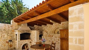 A stone-built outdoor patio with a wooden table and chairs, a stone fireplace, and a wooden ceiling structure. - Villa Argiro in Plaka (Apokoronas)
