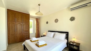 A bedroom with a large wardrobe, a bed with white linens, a bedside table with a lamp, and decorative wall art. - Villa Sakos in Skala (Kefalonia)