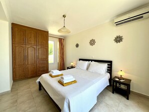 A bedroom with a large wardrobe, a bed with white linens, a bedside table with a lamp, and decorative wall art.