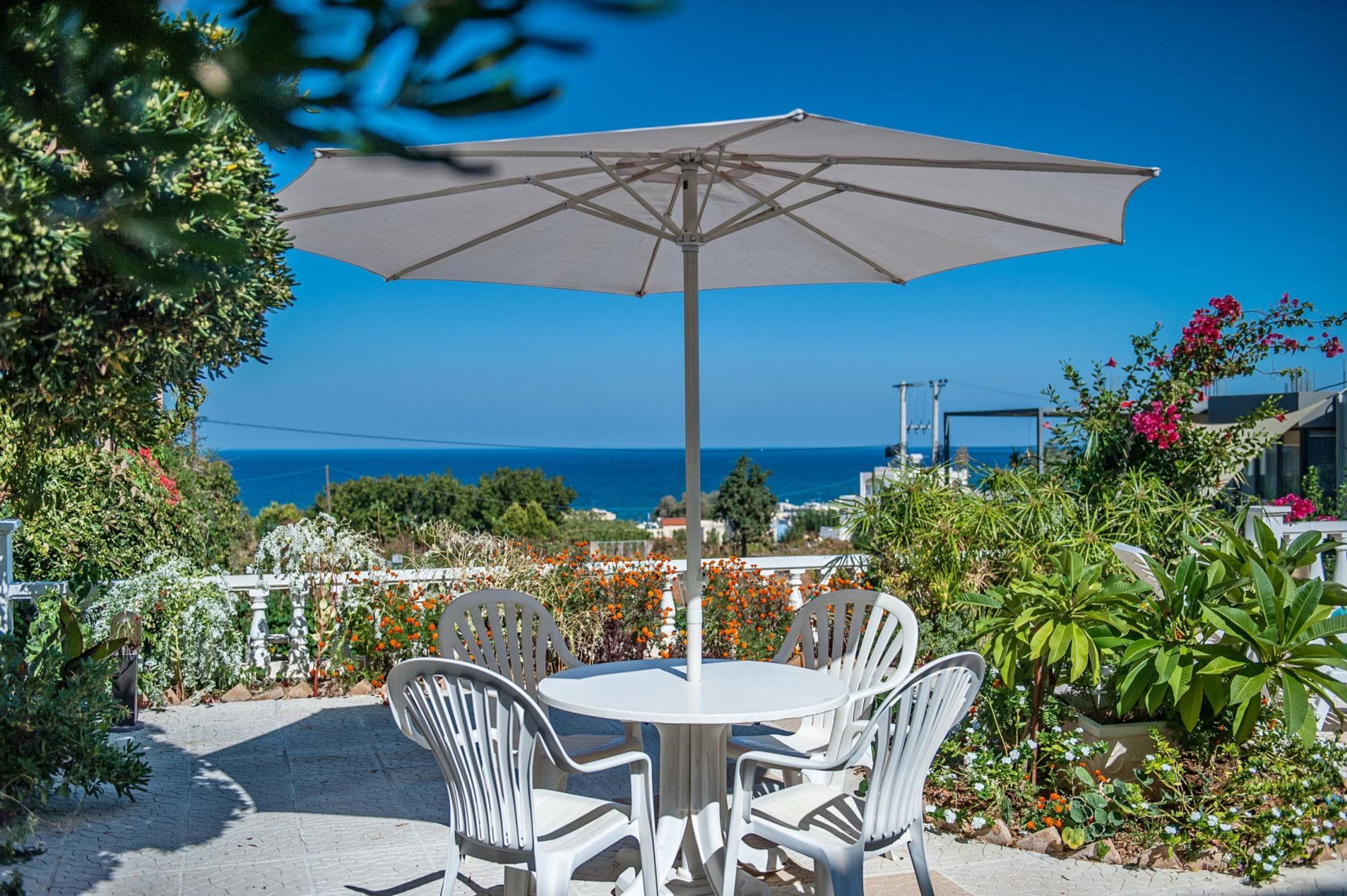 A patio with a round table and four chairs, an umbrella, and a view of the sea.