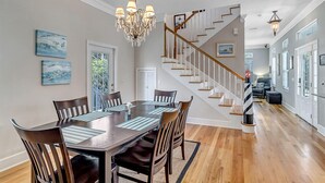 Un espace repas avec une table et des chaises en bois, un lustre et un escalier menant à un autre niveau.