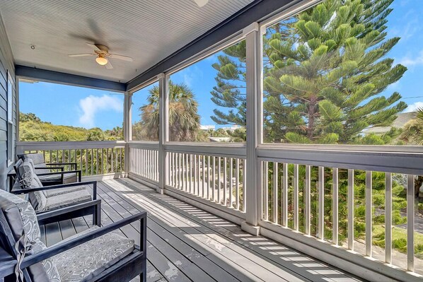 A covered outdoor deck with a ceiling fan, wooden flooring, and a railing.