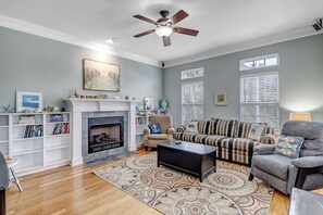 A living room with a fireplace, a ceiling fan, and a patterned rug.