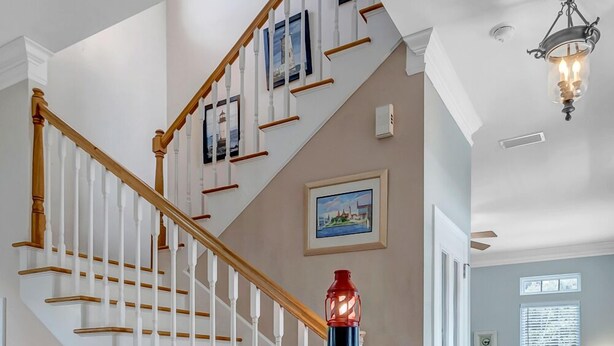 Un escalier avec des balustrades blanches et des rampes en bois, menant à un palier où se trouve un objet à rayures rouges et noires.