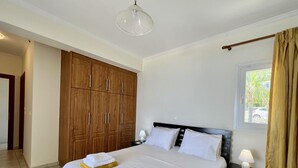 A hotel room with a large bed, wooden wardrobe, and a window with curtains. - Villa Seagull in Skala (Kefalonia)