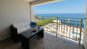A balcony with a white sofa, a small table with a plate of fruit, and a view of the sea. - Villa Seagull in Skala (Kefalonia)