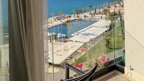 A balcony with a clear view of a pool, palm trees, and a distant cityscape. - Esbjerg Hotel (Vlorë)