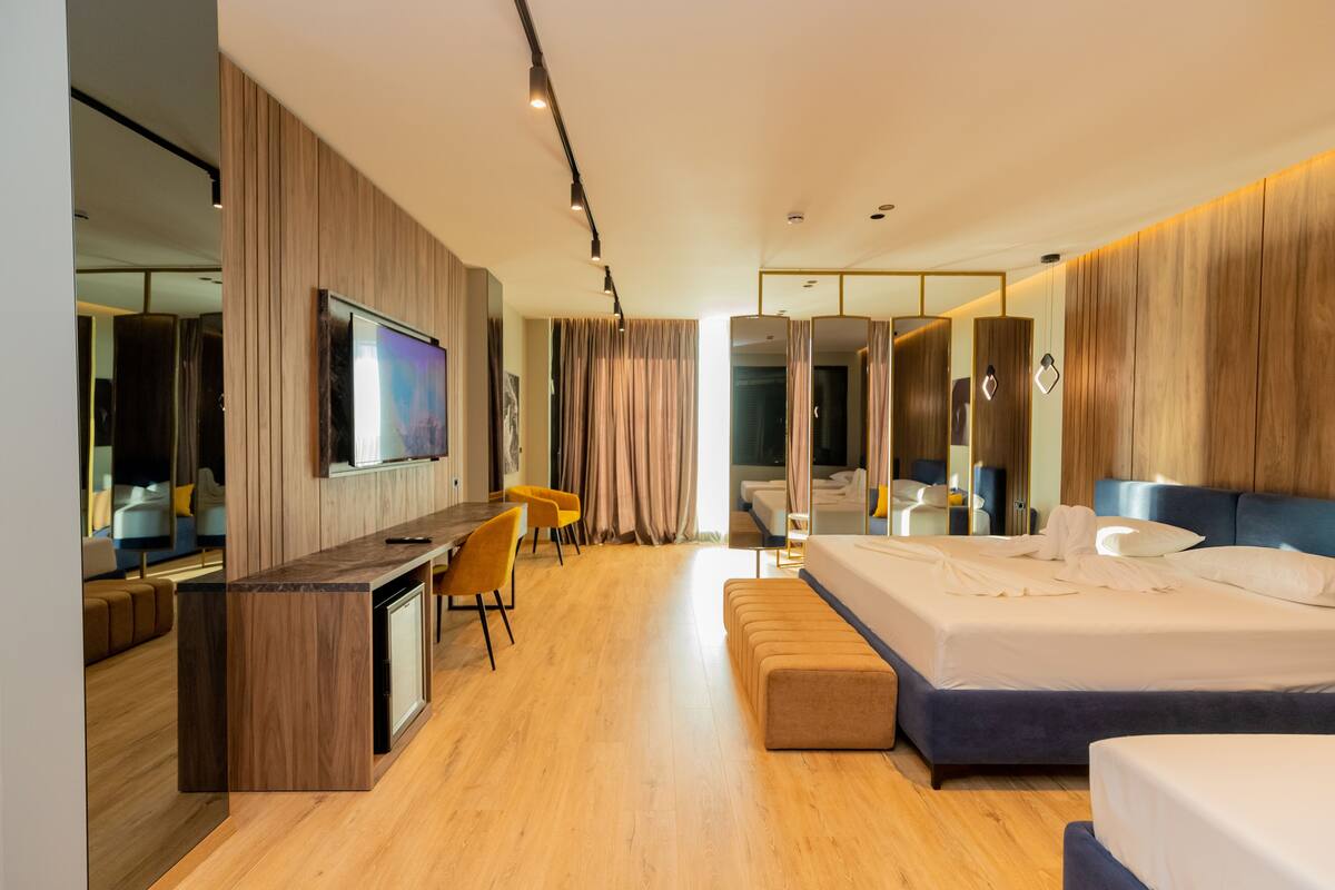 Une chambre d’hôtel moderne avec un plancher en bois, un grand lit, un bureau avec une chaise, une télévision et une salle de bain équipée d’un miroir et d’une douche.
