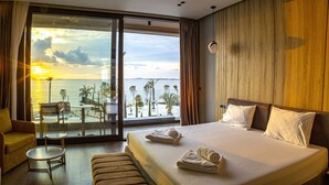 A hotel room with a large bed, a small table, a sofa, and a view of the sea and palm trees. - Esbjerg Hotel (Vlorë)