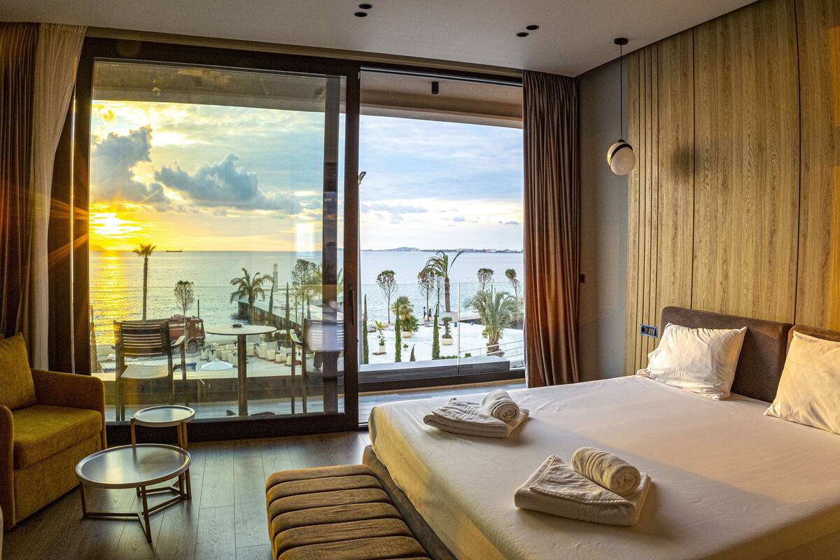 Une chambre d’hôtel avec un grand lit, une petite table, un canapé et une vue sur la mer et les palmiers.